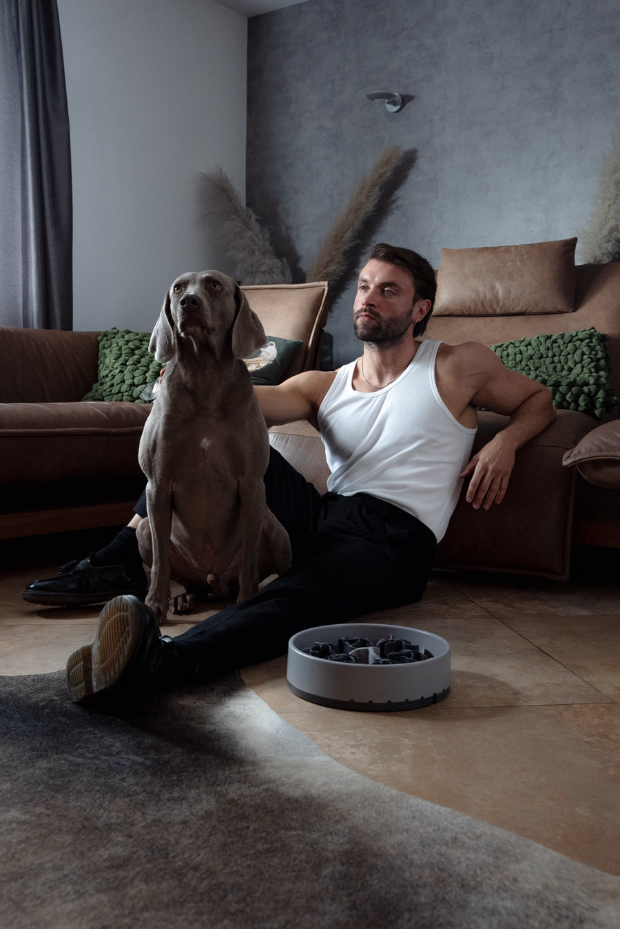 Ein Mann sitzt im Wohnzimmer auf dem Boden neben Weimaraner Hunter, davor steht eine graue SoulBowl